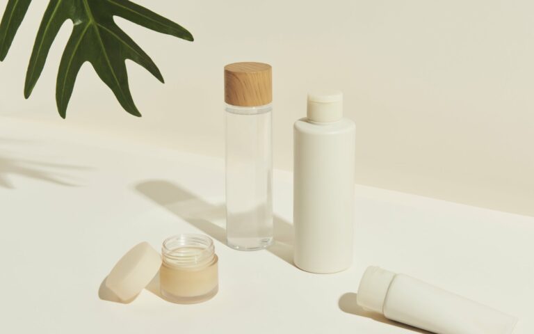 Verschiedene kosmetische Flaschen und Tiegel, darunter ein Glas mit Holzstoß, auf einem hellen Untergrund.