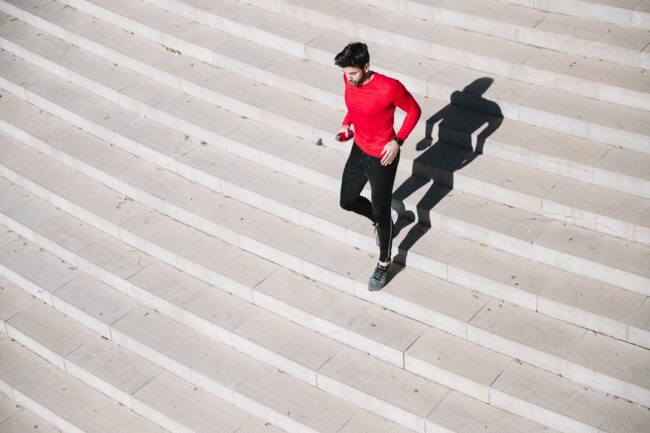 Stiegensteigen_Fitness.jpg Mann in rotem Shirt joggt über eine helle Treppe, sein Schatten ist deutlich sichtbar.