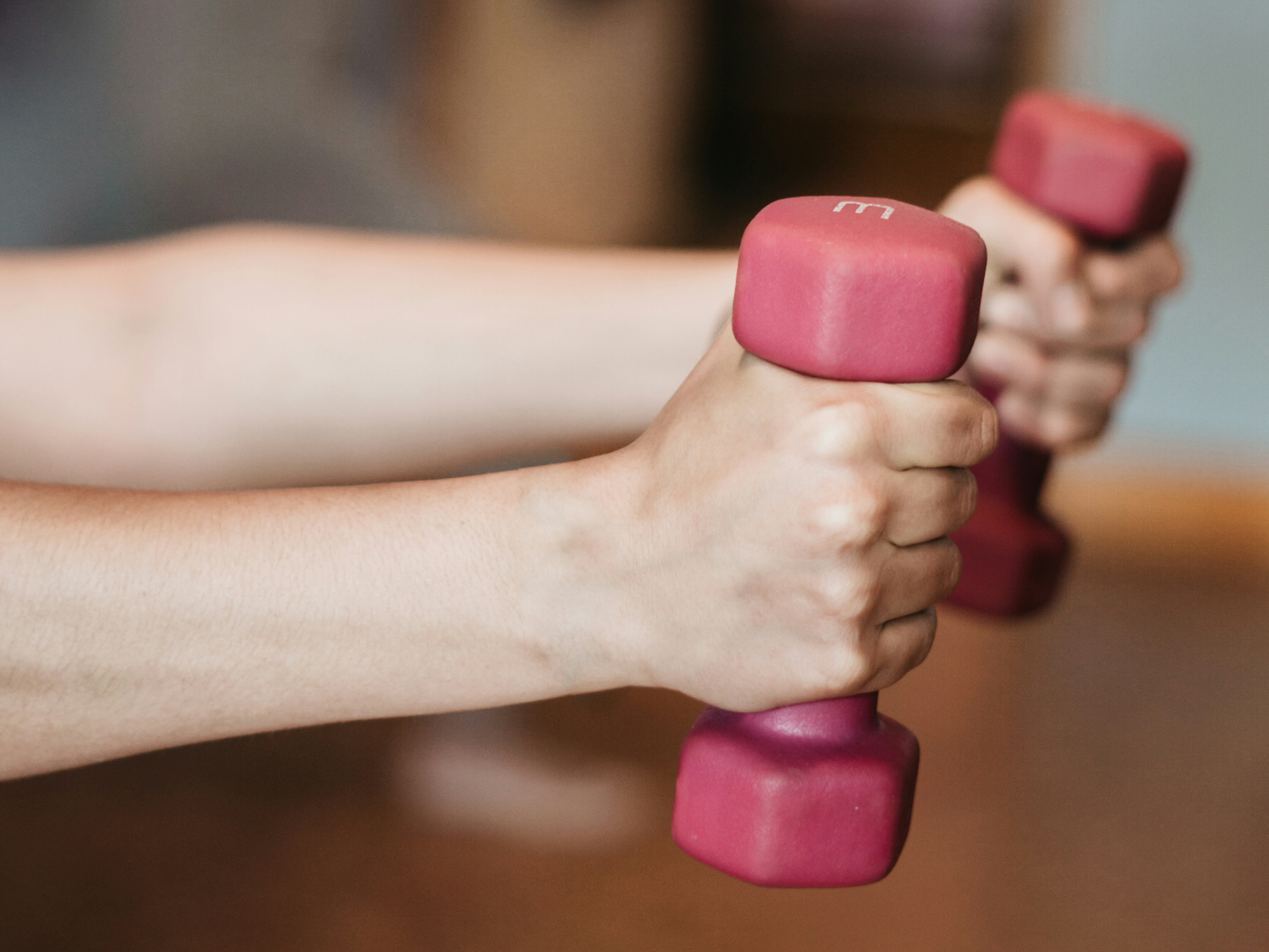 Hände halten zwei pinkfarbene Kurzhanteln in einem Fitnessstudio.