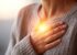 Eine Person in einem grauen Pullover legt die Hand auf ihr Herz, umgeben von warmem Licht.