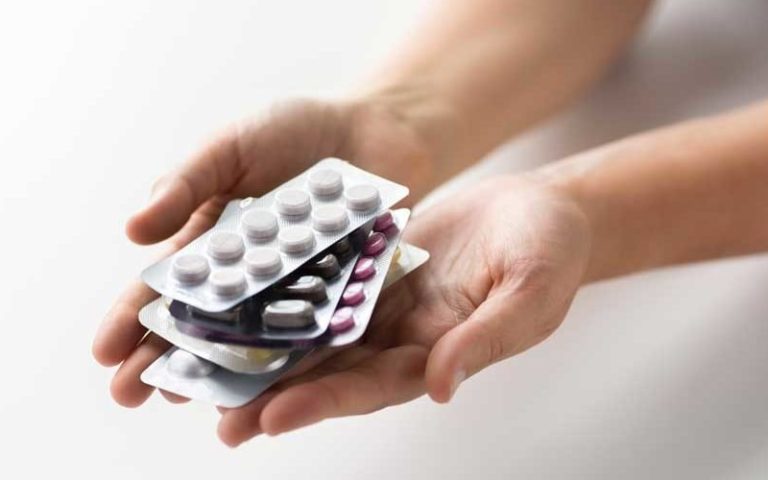 Hände halten mehrere Blisterverpackungen mit unterschiedlichen Tabletten in verschiedenen Farben.