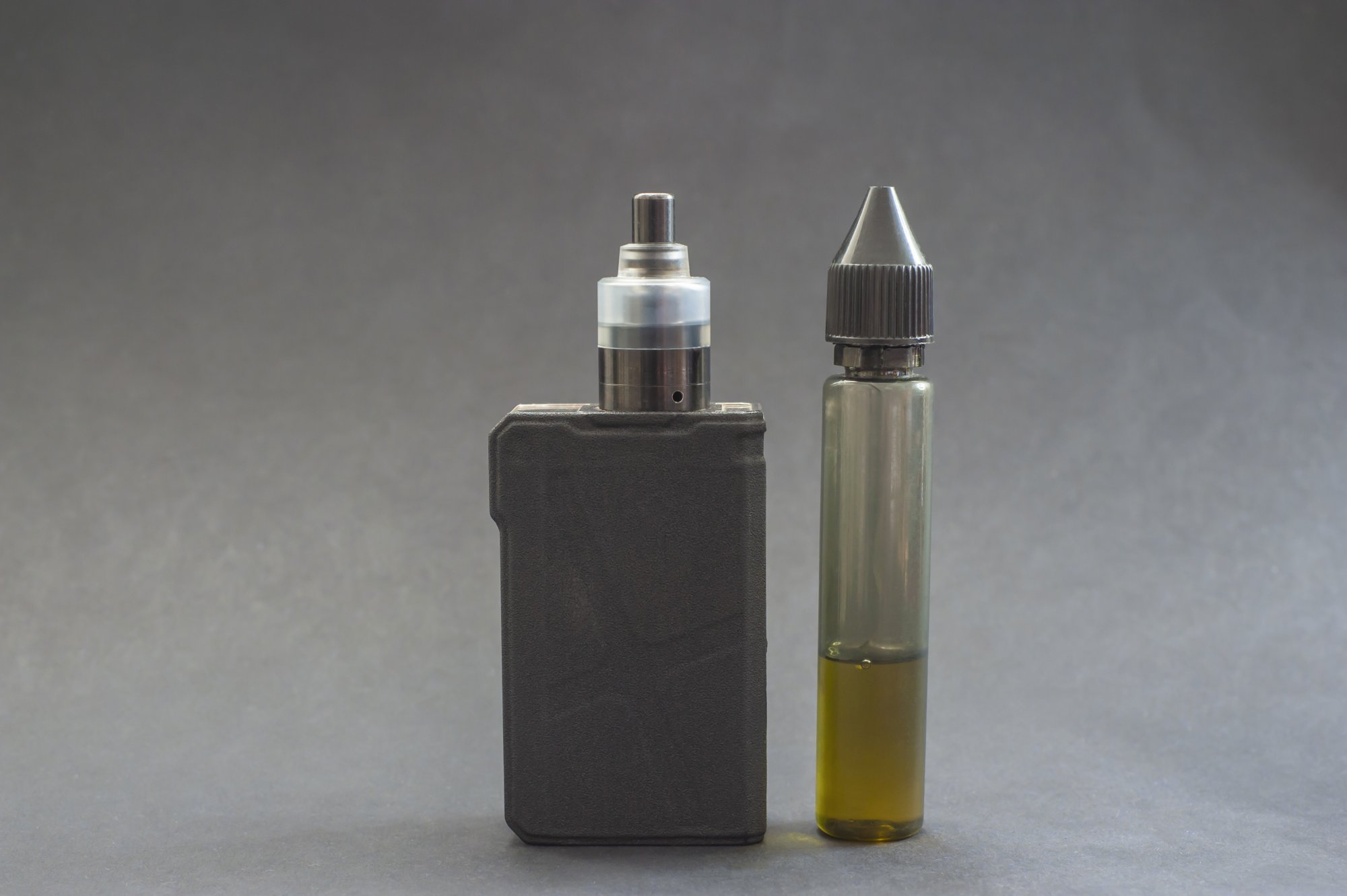 e-zigarette.jpg Ein Verdampfergerät links, daneben eine Flasche mit E-Liquid in einer transparenten Verpackung.