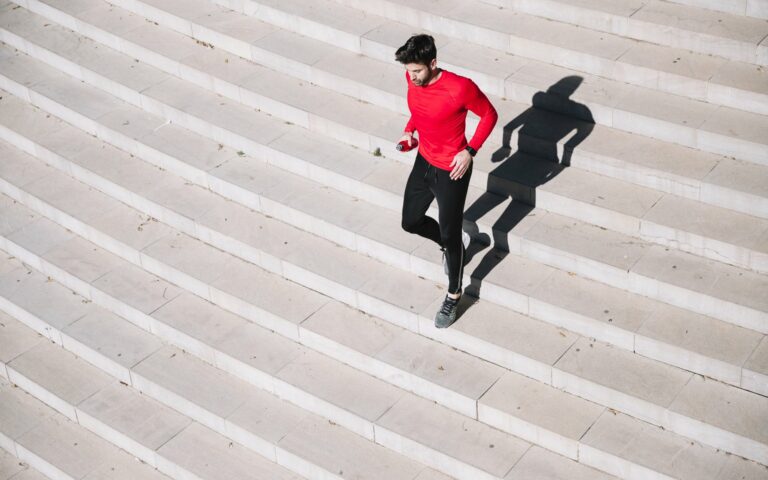 Mann in rotem Shirt joggt über eine helle Treppe, sein Schatten ist deutlich sichtbar.