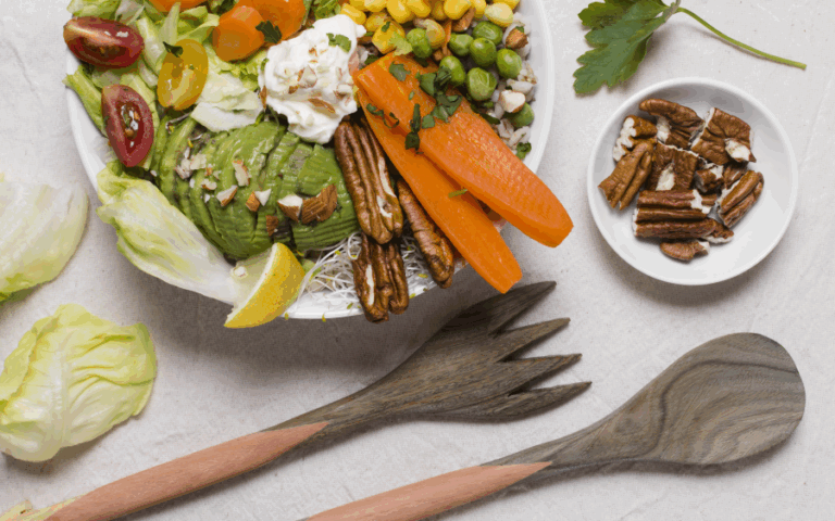 Bunte Salatschüssel mit Avocado, Karotten, Erbsen, Mais, Tomaten und Nüssen, begleitet von Holzbesteck und einer Schale Nüssen.