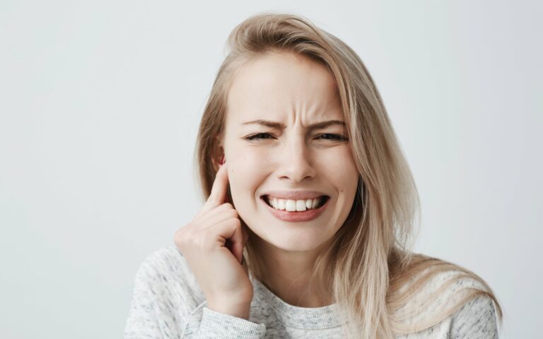 Junge Frau mit schmerzverzerrtem Gesicht, hält sich den rechten Ohrbereich mit der Hand.