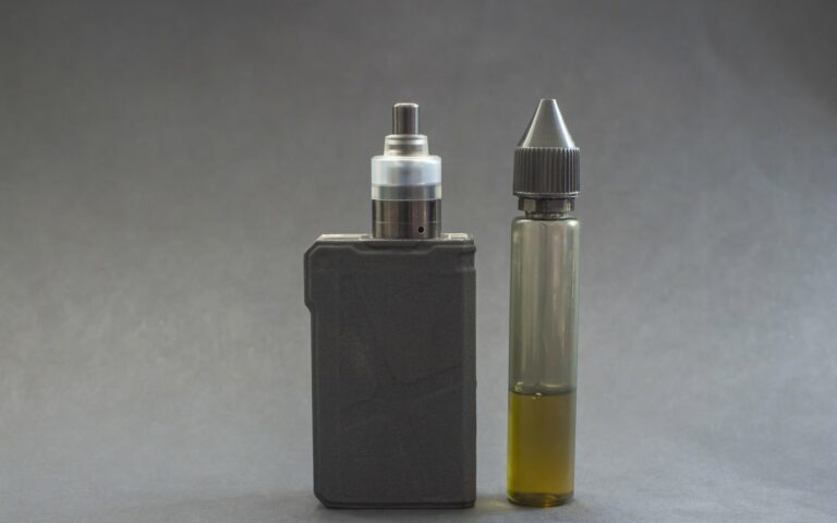 Ein Verdampfergerät links, daneben eine Flasche mit E-Liquid in einer transparenten Verpackung.