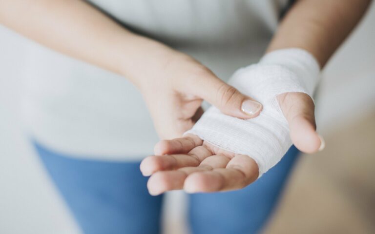 Händedetail mit einer verbundenen Hand, die eine sanfte Verletzung zeigt, während die andere Hand sie festhält.